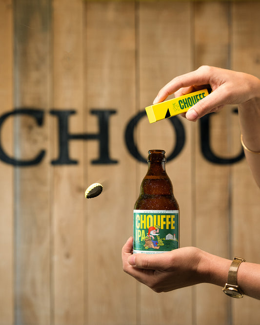 hand holding Chouffe IPA and opening with yellow Chouffe bottle opener