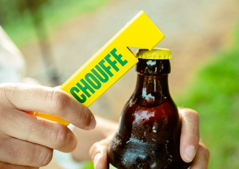 hand holding yellow Chouffe bottle opener opening a bottle